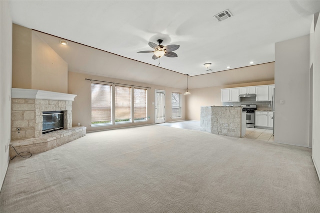 unfurnished living room featuring light carpet, ceiling fan, and a stone fireplace