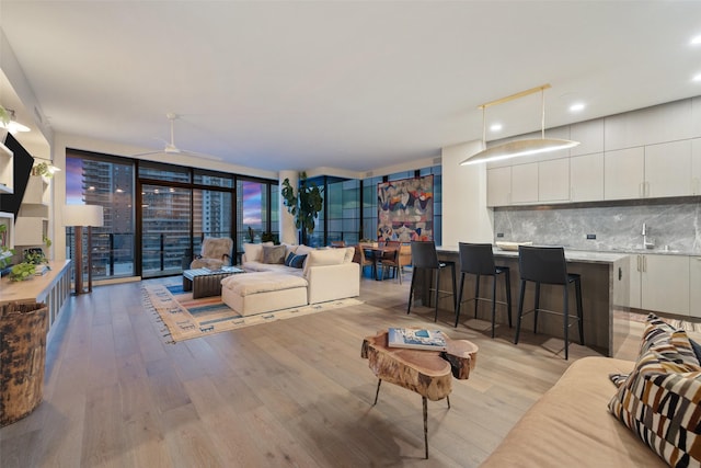 living room with sink, ceiling fan, expansive windows, and light hardwood / wood-style flooring