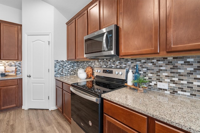 kitchen with stainless steel appliances, light stone countertops, light hardwood / wood-style flooring, and decorative backsplash