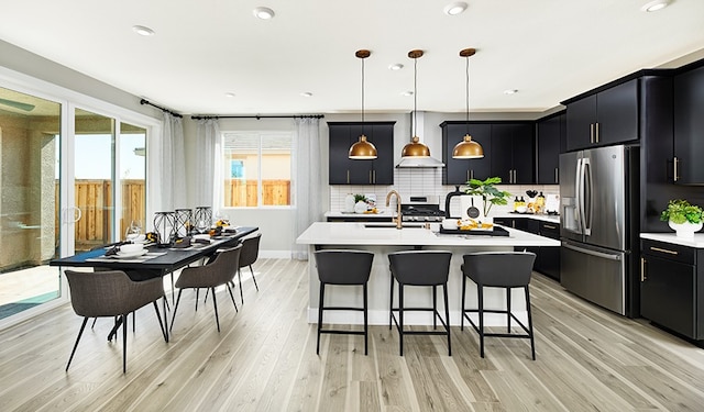 kitchen with hanging light fixtures, stainless steel appliances, sink, and a center island with sink