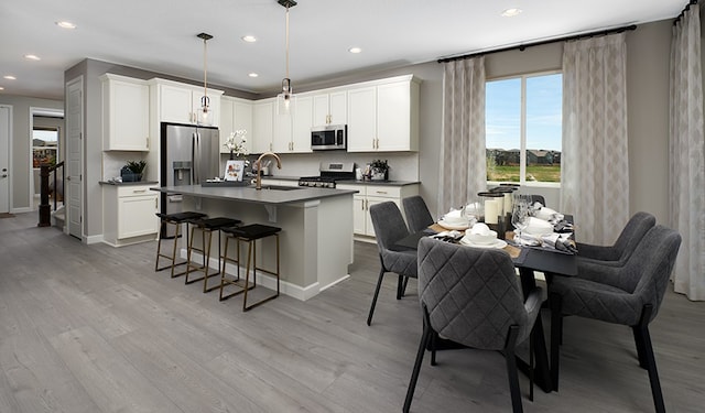 kitchen with sink, appliances with stainless steel finishes, light hardwood / wood-style floors, white cabinets, and decorative light fixtures