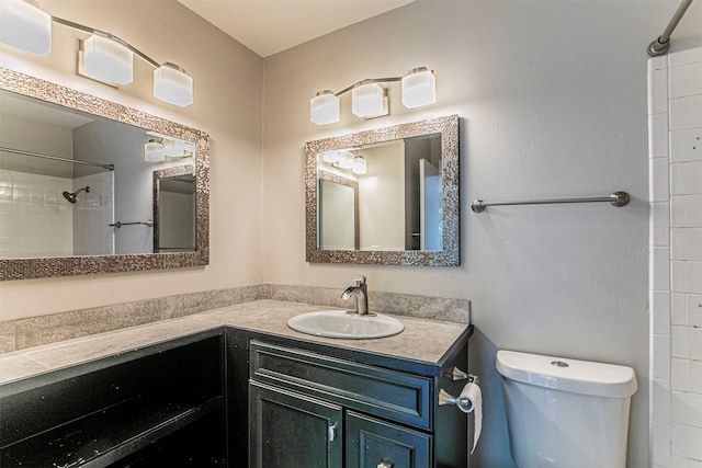 bathroom with toilet, vanity, and tiled shower