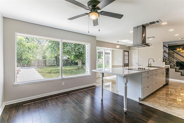 kitchen with white cabinets, island range hood, a center island with sink, black electric cooktop, and sink