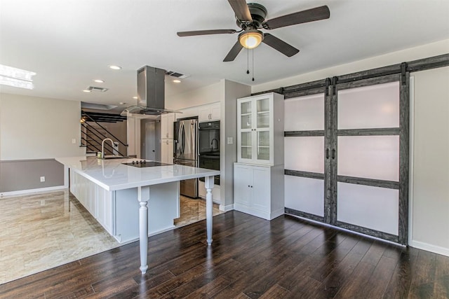 kitchen with a barn door, island range hood, black appliances, a kitchen bar, and white cabinetry