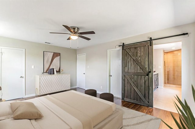 bedroom with a barn door, baseboards, visible vents, a ceiling fan, and wood finished floors