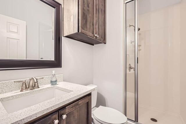 bathroom featuring a shower with shower door, toilet, and vanity