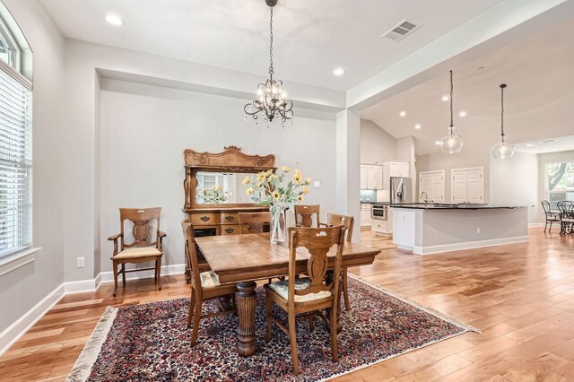 dining space featuring sink, vaulted ceiling, an inviting chandelier, and light wood-type flooring