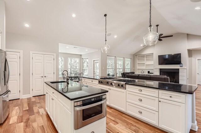 kitchen with white cabinets, appliances with stainless steel finishes, lofted ceiling, a kitchen island, and hanging light fixtures