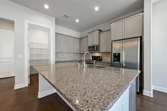 kitchen with appliances with stainless steel finishes, light stone counters, sink, and a spacious island