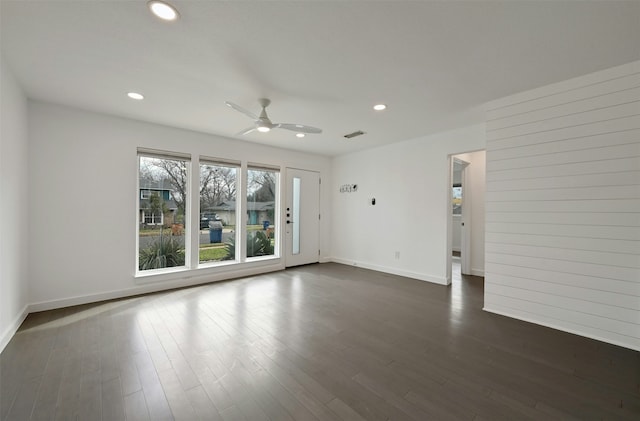 empty room featuring ceiling fan, dark wood-type flooring, and wood walls