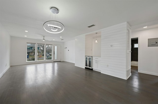 unfurnished living room with ceiling fan with notable chandelier, dark hardwood / wood-style flooring, and wood walls