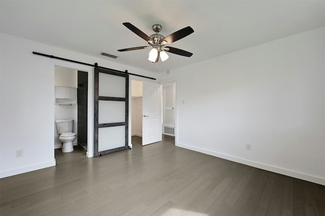 unfurnished bedroom with ceiling fan, connected bathroom, a barn door, and wood-type flooring