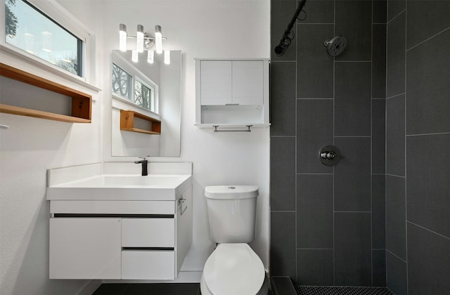 bathroom with a tile shower, vanity, and toilet