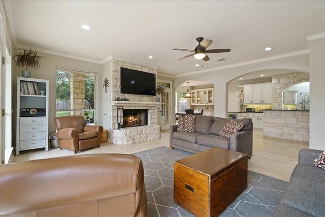 living room featuring crown molding, a stone fireplace, and ceiling fan