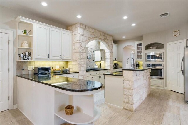 kitchen featuring white cabinets, decorative backsplash, a kitchen island with sink, kitchen peninsula, and stainless steel appliances