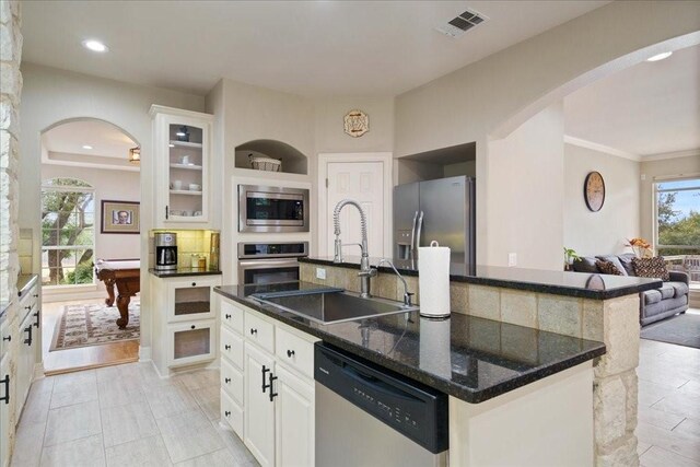 kitchen with sink, stainless steel appliances, an island with sink, white cabinets, and dark stone counters