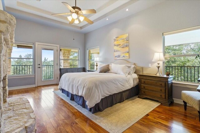 bedroom featuring ceiling fan, wood-type flooring, access to exterior, and a raised ceiling