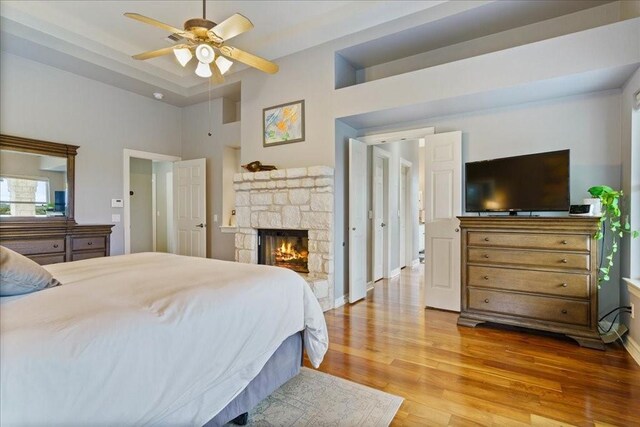 bedroom featuring hardwood / wood-style flooring, a fireplace, ceiling fan, and a high ceiling