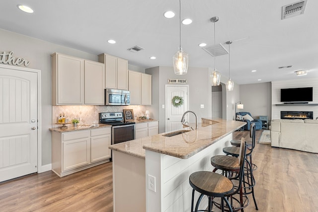 kitchen featuring a center island with sink, stainless steel appliances, decorative light fixtures, light stone counters, and sink