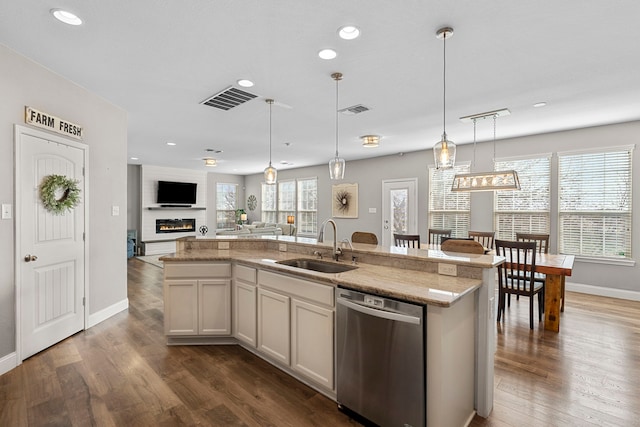 kitchen featuring dishwasher, a large fireplace, sink, hanging light fixtures, and a kitchen island with sink