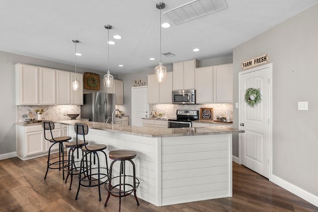 kitchen featuring decorative light fixtures, a kitchen bar, an island with sink, stainless steel appliances, and white cabinets