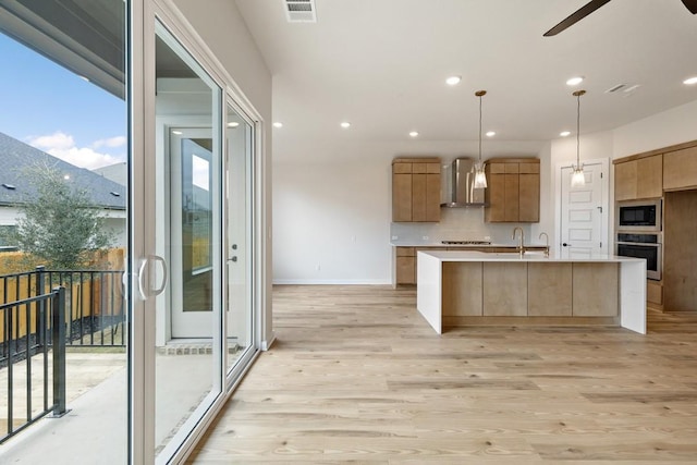 kitchen featuring wall chimney exhaust hood, hanging light fixtures, a center island with sink, built in microwave, and oven