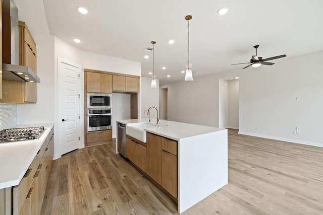 kitchen featuring pendant lighting, stainless steel appliances, a kitchen island with sink, ceiling fan, and sink