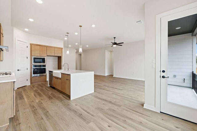 kitchen featuring a kitchen island with sink, stainless steel appliances, hanging light fixtures, ceiling fan, and light hardwood / wood-style flooring