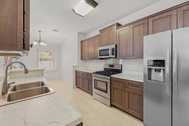 kitchen featuring light stone counters, hanging light fixtures, stainless steel appliances, a notable chandelier, and sink