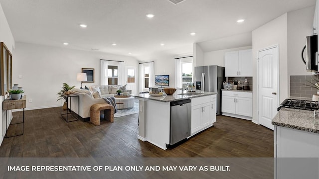 kitchen featuring stainless steel appliances, light stone countertops, white cabinets, and an island with sink