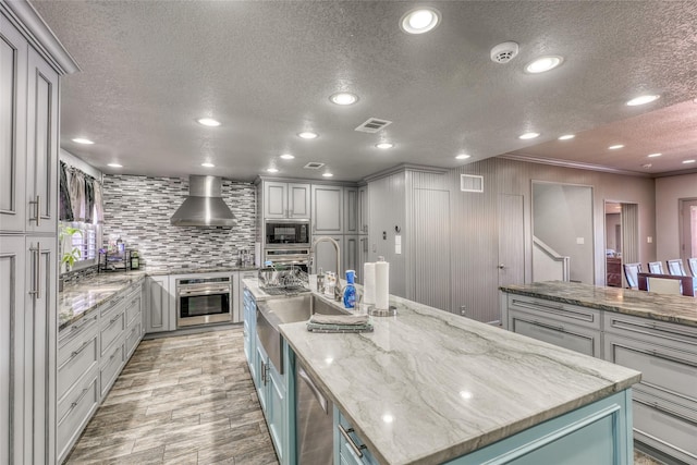 kitchen featuring stainless steel appliances, a large island, light stone countertops, wall chimney range hood, and crown molding