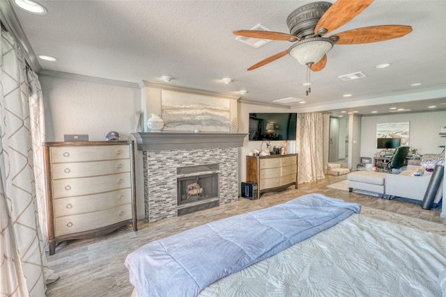 bedroom featuring a fireplace, a textured ceiling, ceiling fan, light hardwood / wood-style flooring, and crown molding