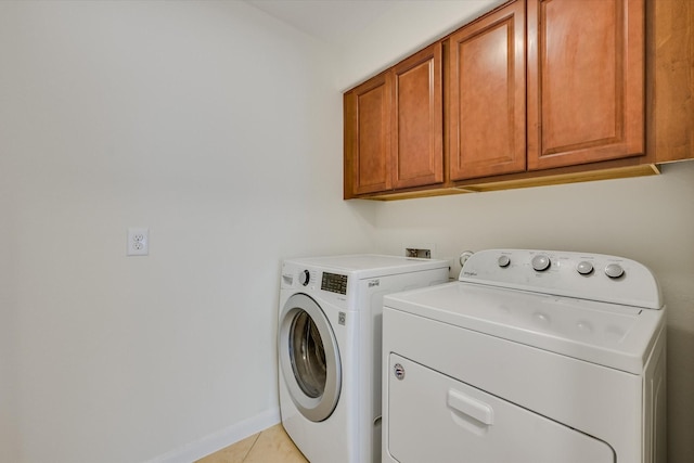 clothes washing area with light tile patterned floors, washer and dryer, and cabinets