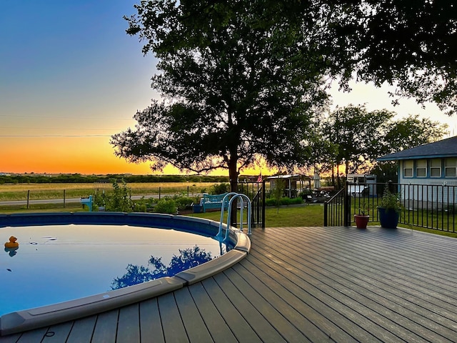 pool at dusk featuring a deck and a lawn