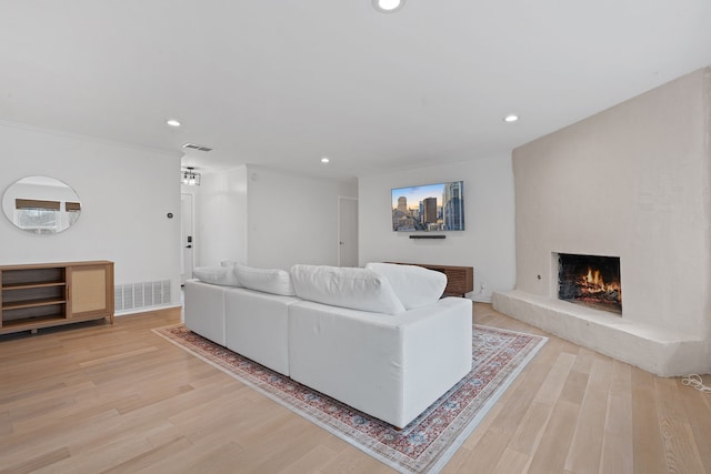 living room with a large fireplace, light hardwood / wood-style floors, and ornamental molding