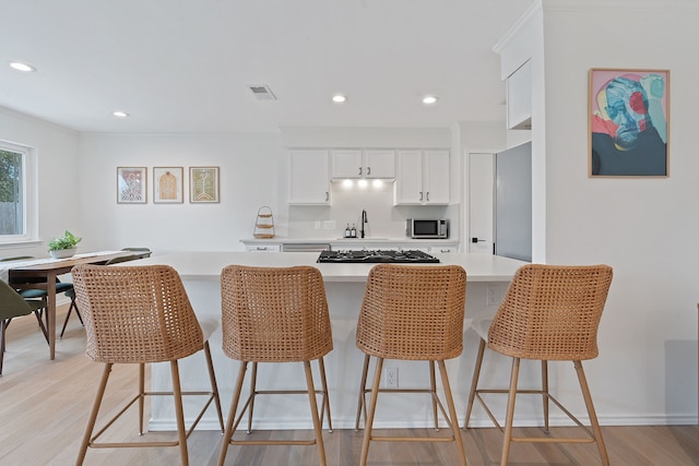 kitchen featuring sink, white cabinets, a kitchen bar, light hardwood / wood-style floors, and appliances with stainless steel finishes