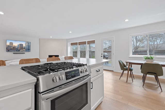 kitchen with gas range, white cabinets, light wood-type flooring, and crown molding