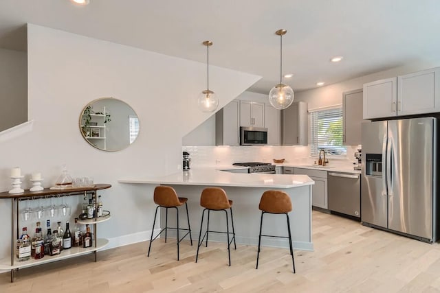 kitchen with decorative light fixtures, a breakfast bar, gray cabinetry, appliances with stainless steel finishes, and sink