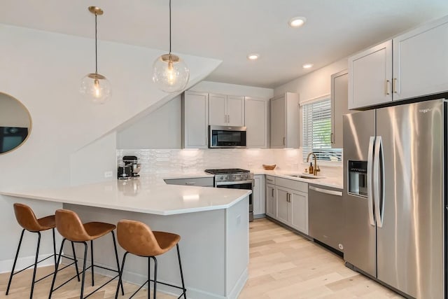 kitchen featuring light hardwood / wood-style floors, kitchen peninsula, hanging light fixtures, a breakfast bar, and appliances with stainless steel finishes