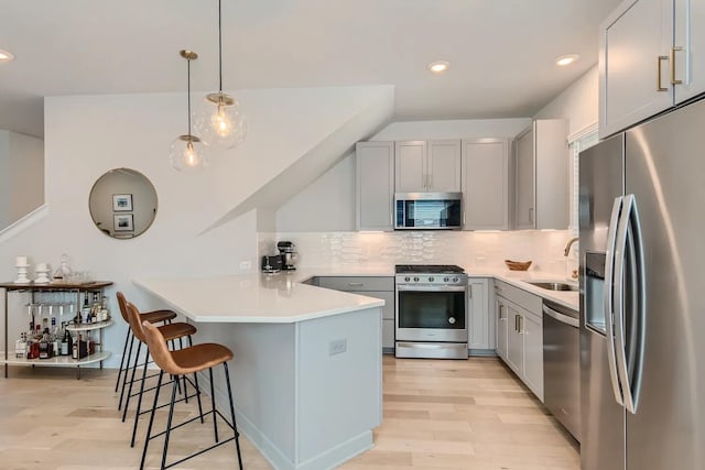 kitchen with gray cabinets, appliances with stainless steel finishes, kitchen peninsula, sink, and decorative light fixtures