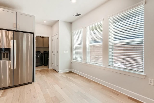 kitchen with light hardwood / wood-style flooring, washing machine and dryer, and stainless steel refrigerator with ice dispenser