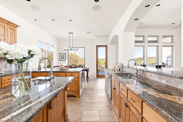 kitchen featuring tasteful backsplash, dark stone counters, hanging light fixtures, and sink