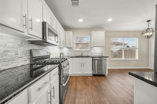 kitchen featuring decorative light fixtures, white cabinets, dark stone counters, a notable chandelier, and appliances with stainless steel finishes