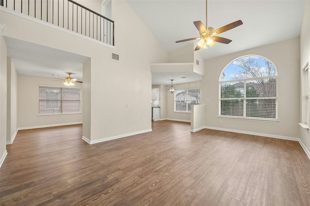 unfurnished living room with hardwood / wood-style floors, high vaulted ceiling, and ceiling fan with notable chandelier