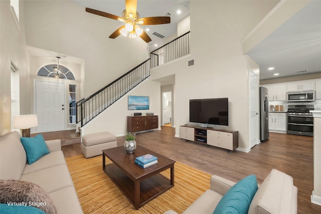 living room featuring a high ceiling, light wood-type flooring, and ceiling fan with notable chandelier