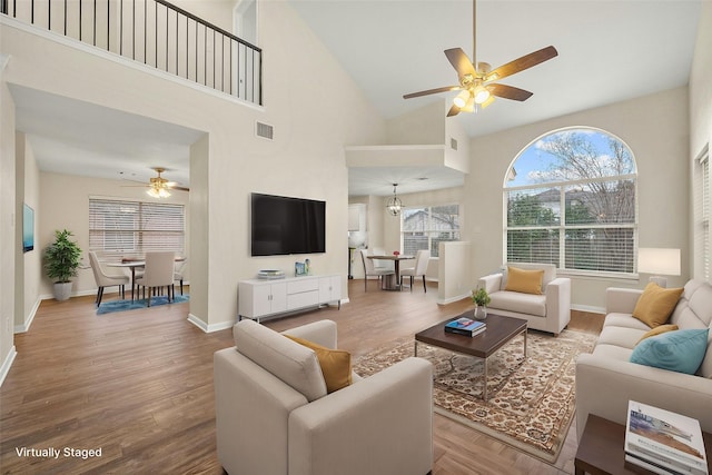 living room featuring a towering ceiling, hardwood / wood-style flooring, and ceiling fan with notable chandelier