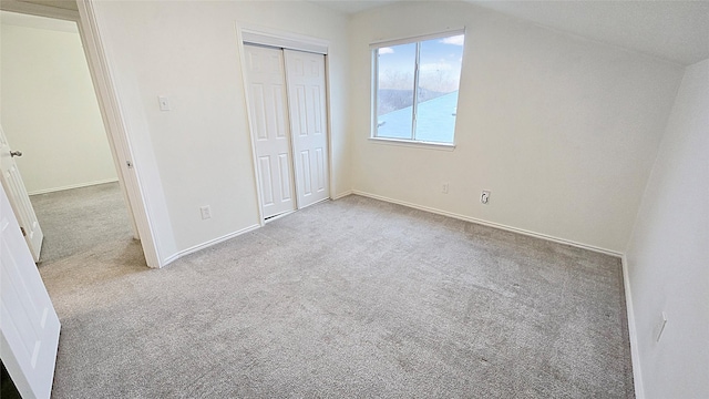 unfurnished bedroom featuring a closet, light carpet, and lofted ceiling