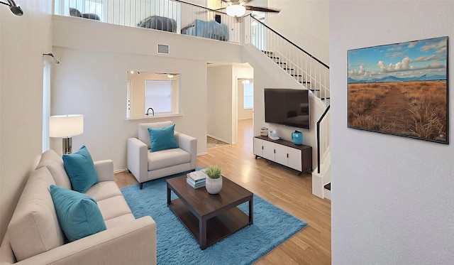 living room with a high ceiling, ceiling fan, and wood-type flooring