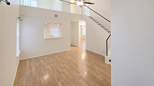 unfurnished living room with a high ceiling, ceiling fan, and light hardwood / wood-style floors