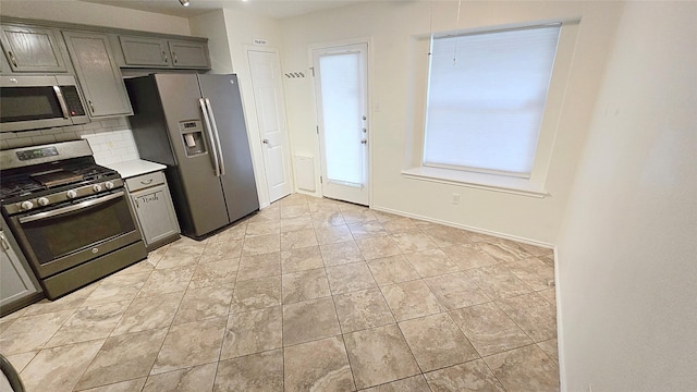 kitchen with appliances with stainless steel finishes, light tile patterned flooring, gray cabinets, and decorative backsplash